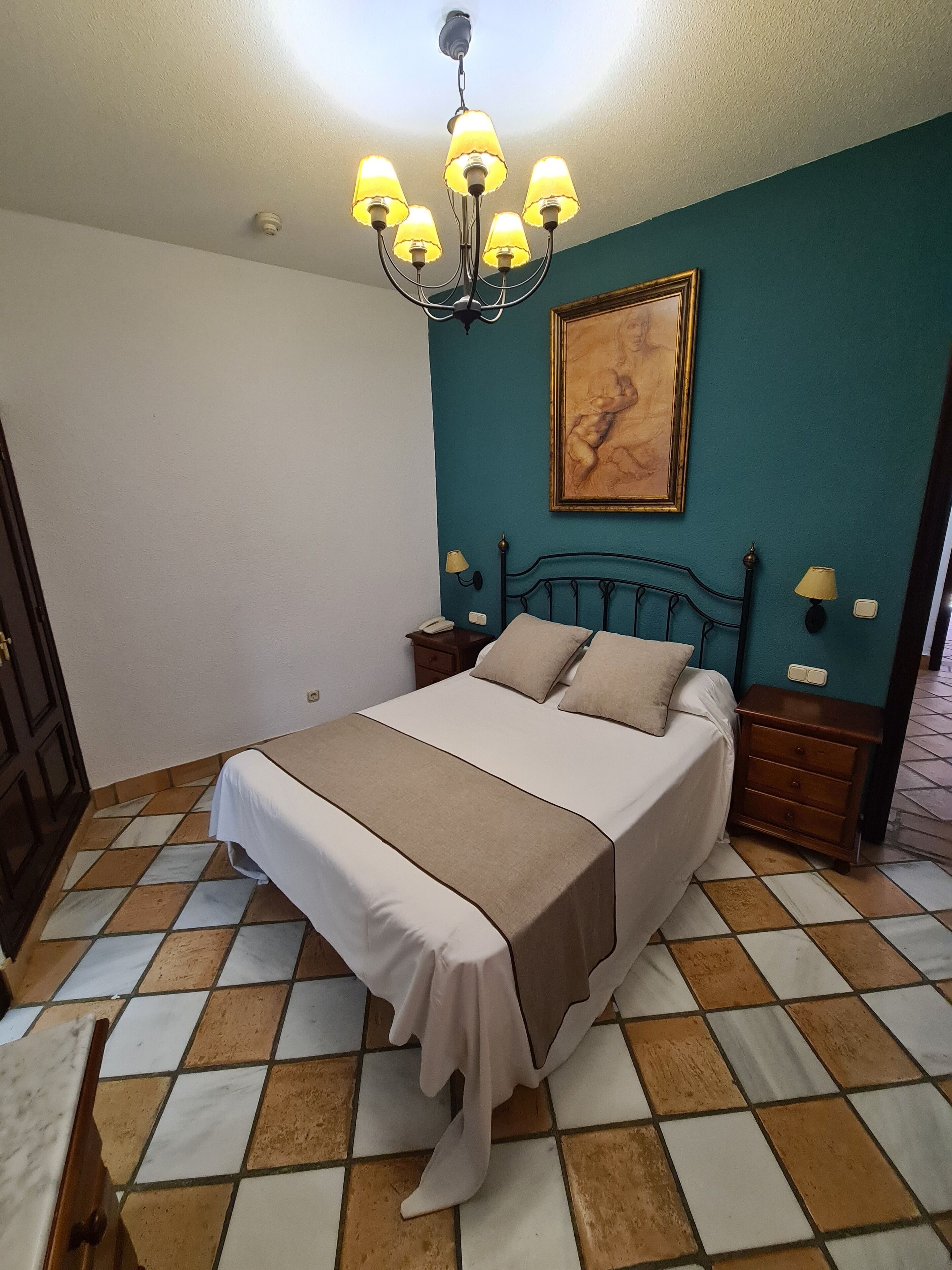 Un dormitorio con una cama, una araña, un cuadro y suelo de baldosas.