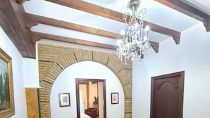A room with a brown sofa, a chandelier, a wooden ceiling, and a tiled floor.