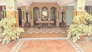 A lobby with a checkered floor, a central table with flowers, and two potted plants.