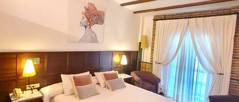 A hotel room with a large bed, two bedside tables with lamps, a chair, a window with curtains, and a painting on the wall.