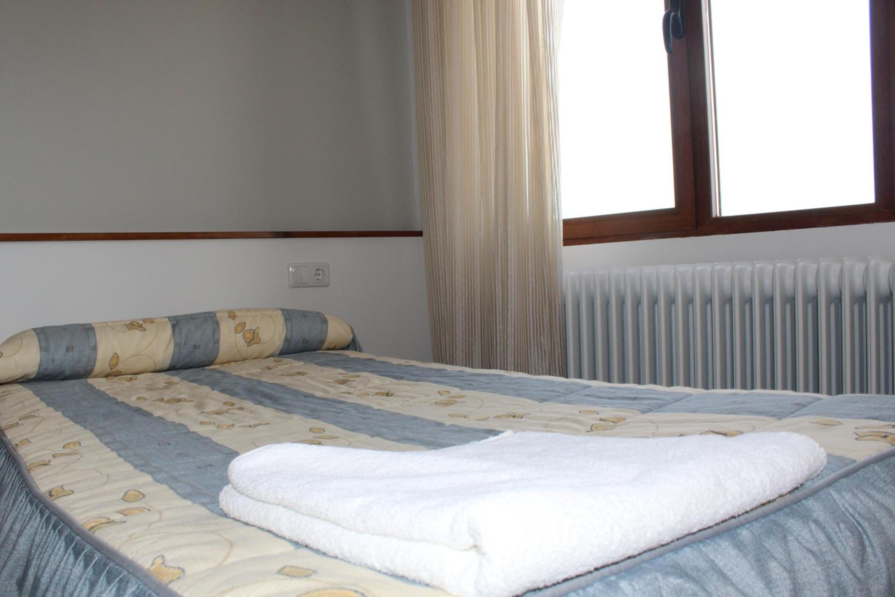 Een net opgemaakt bed met een bedspread met patroon en een witte handdoek.
