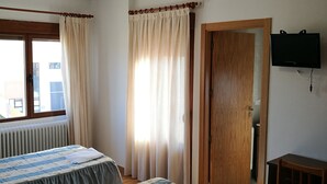 Una habitación de hotel con dos camas, una puerta de madera, un televisor y una ventana con cortinas.