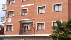 Un edificio de ladrillo de varios pisos, con múltiples ventanas, un balcón y un letrero que indica que es un albergue.