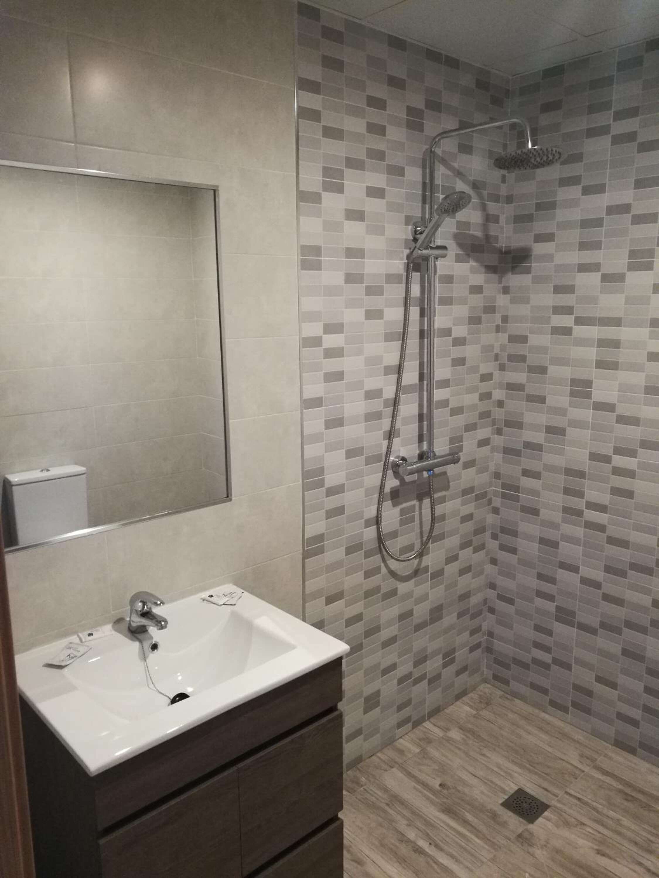 A modern bathroom with a white sink, a mirror, and a shower with a tiled wall.