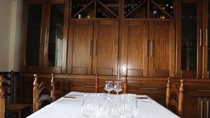 Una mesa de comedor lista, con copas de vino, sillas de madera y un mantel blanco.