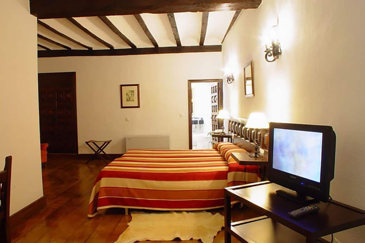 A room with a bed, a television, a remote control, and a wooden floor.