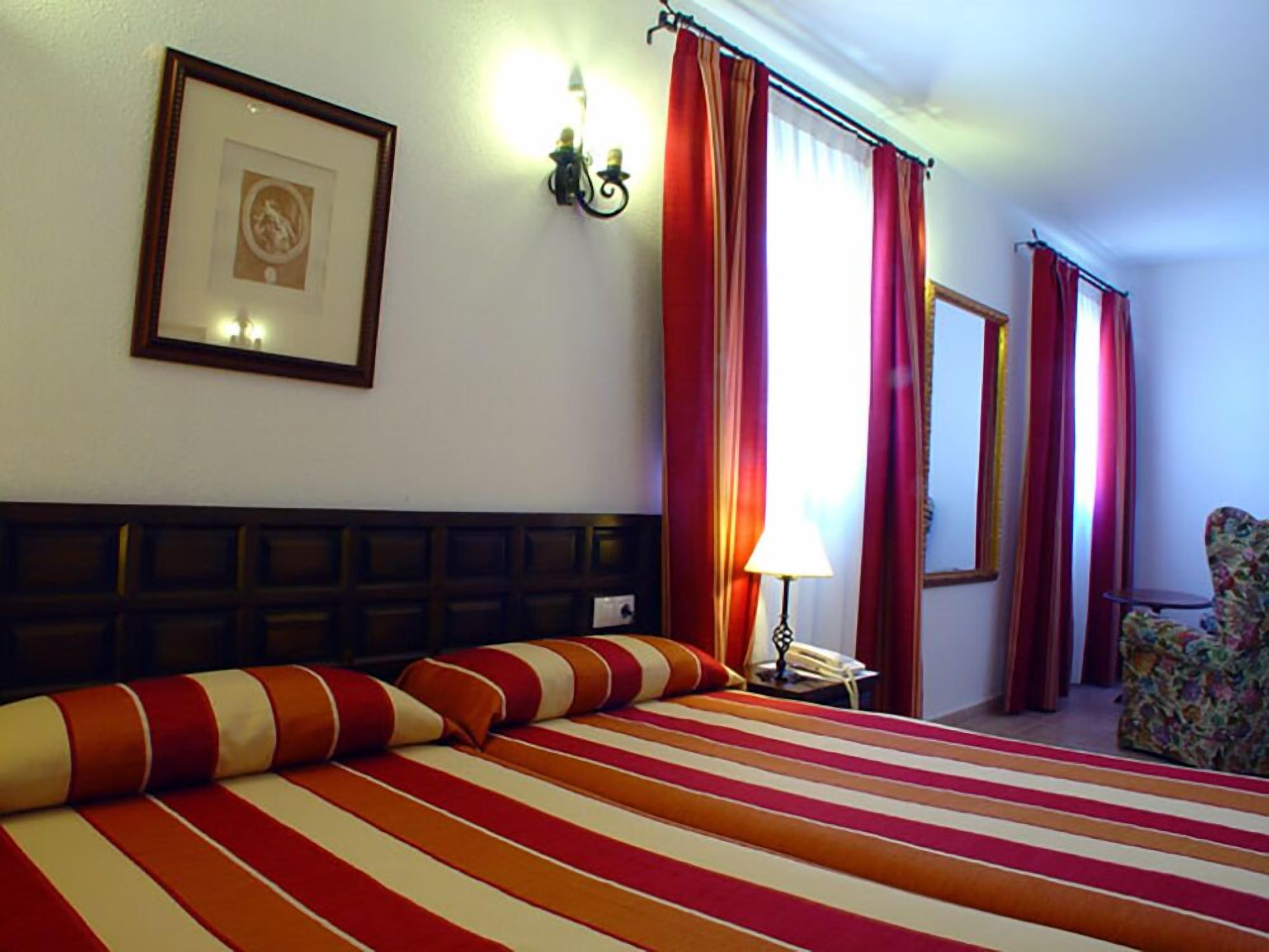 Une chambre d’hôtel avec un grand lit, une literie à rayures, une tête de lit, un tableau encadré, une lampe fixée au mur et une chaise.