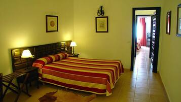 Habitación de hotel con una cama grande, dos lámparas de noche, un cabecero de madera, un cuadro enmarcado en la pared y una puerta que da a otra habitación.