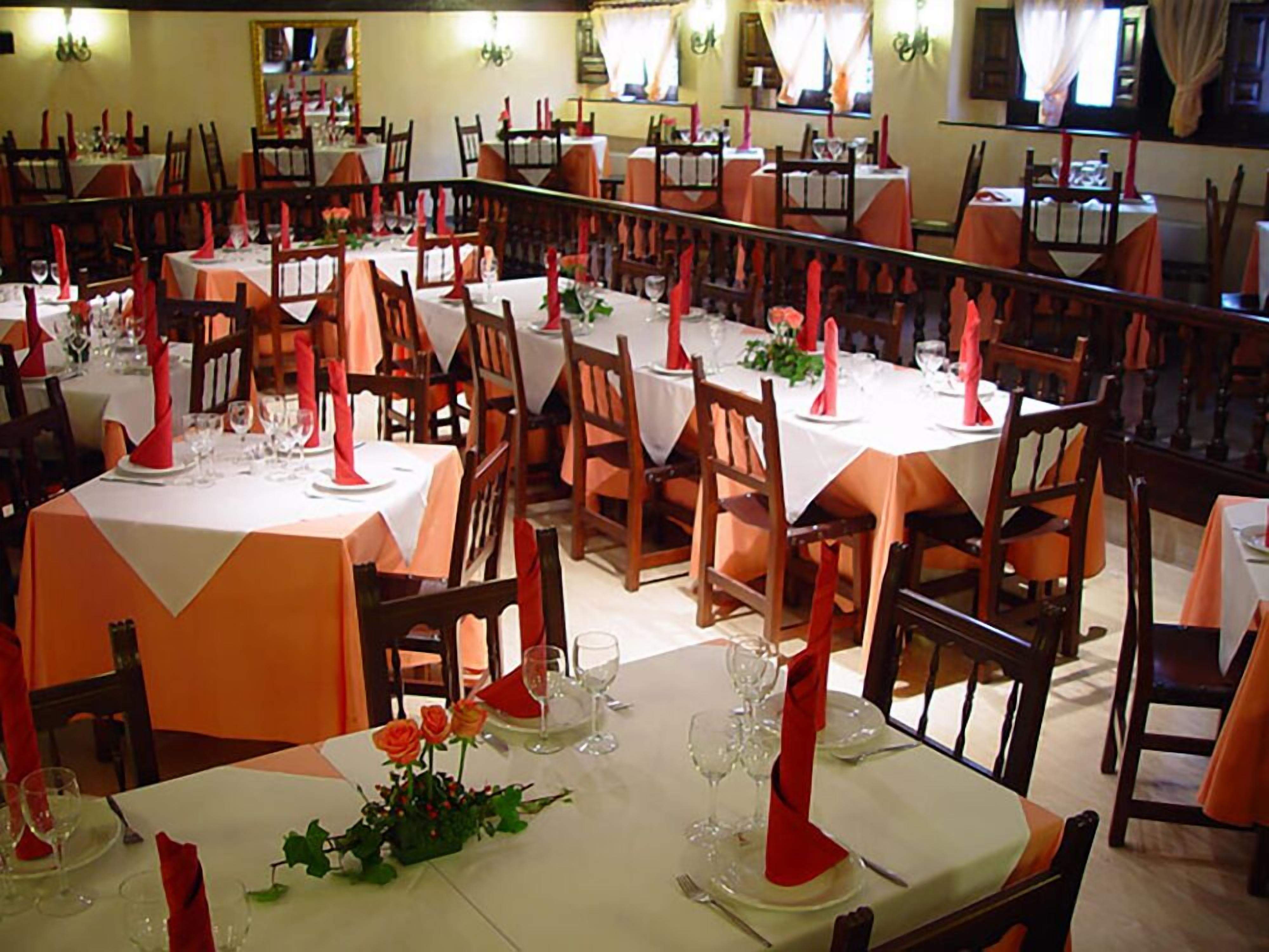 A restaurant with multiple tables set for dining, each with white tablecloths and red napkins.