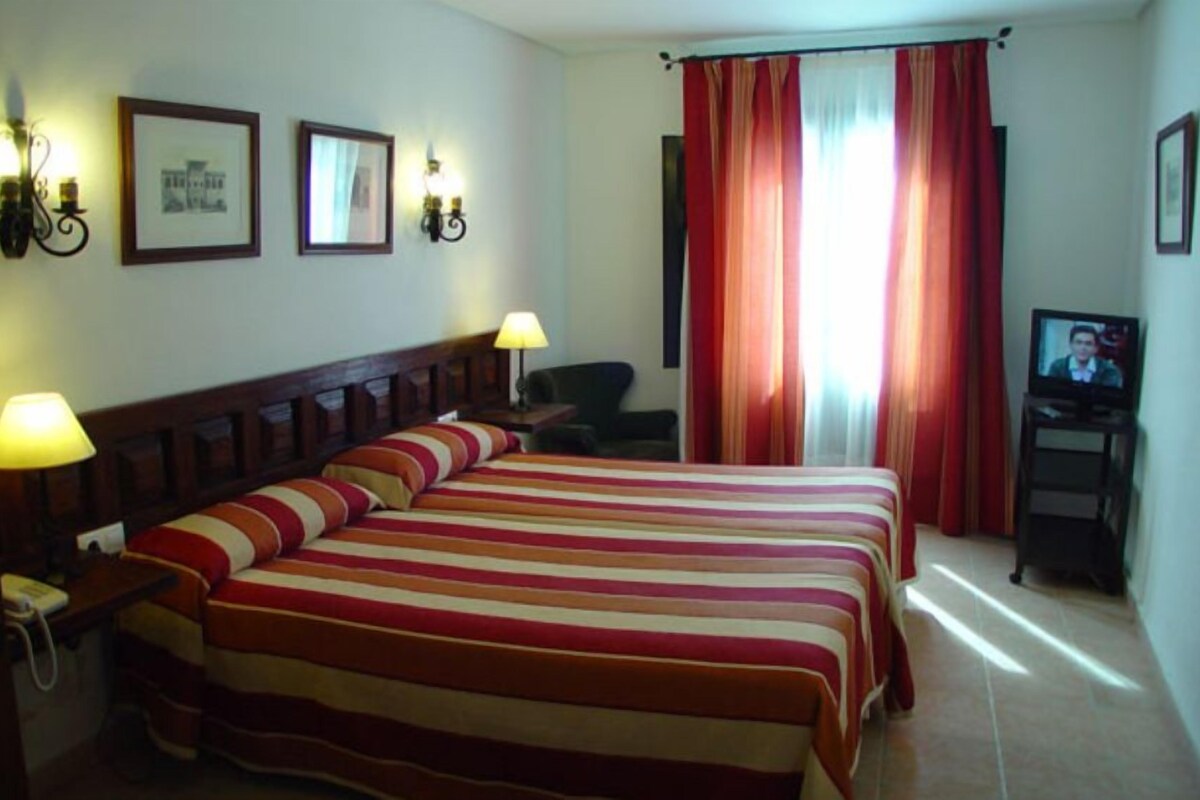 Habitación de hotel con dos camas, un escritorio, una silla, un televisor y cortinas.