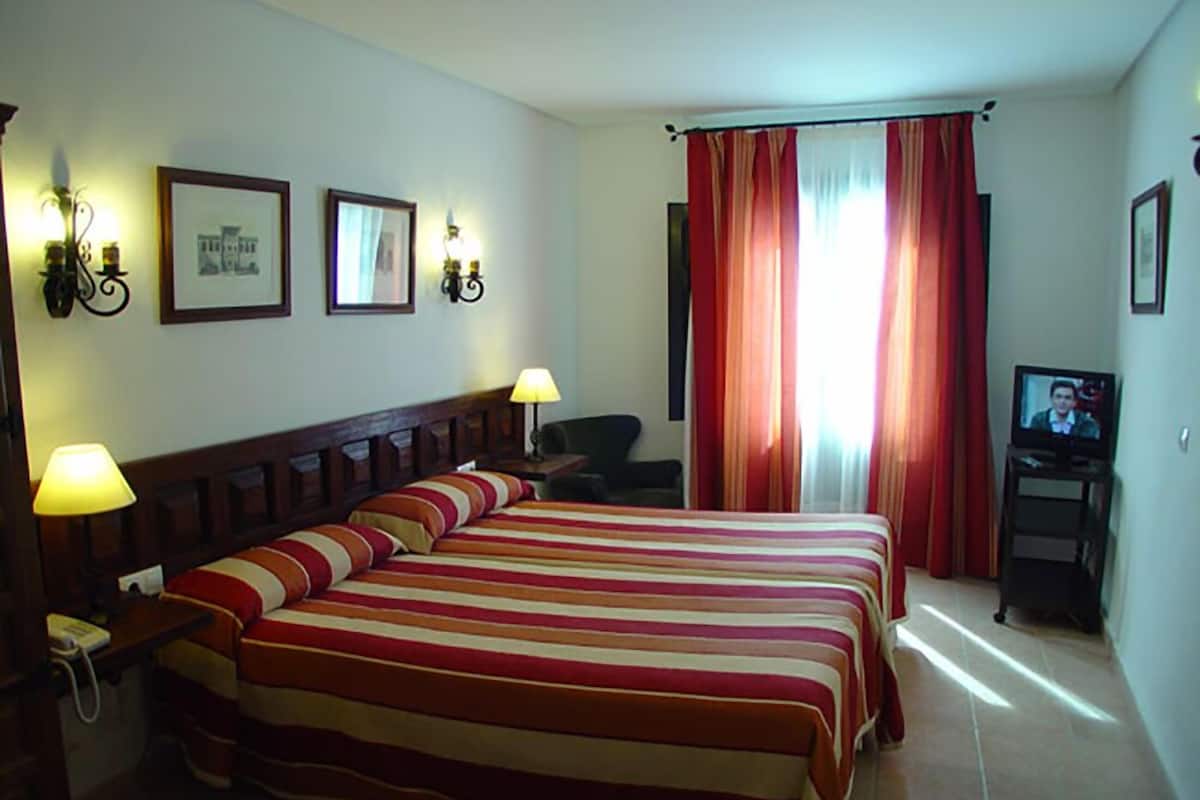 A hotel room with a large bed, two bedside lamps, a television, and a desk with a chair.