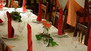 A long dining table set with red napkins, clear glassware, and orange roses. - Nuevo Arlanza (Covarrubias)