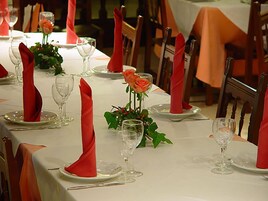 A long dining table set with red napkins, clear glassware, and orange roses.
