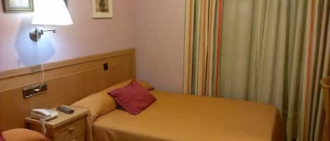A hotel room with a bed, a bedside table with a lamp, a phone, and a small table with a vase.