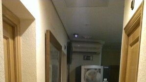 A narrow hallway with beige walls and wooden doors. A refrigerator is visible in the background, and there is a small shelf with items on it. - Hostal Cruz Sol (Madrid)