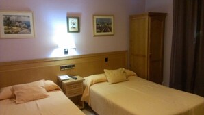 A hotel room with two beds, a nightstand, a lamp, and a wardrobe. - Hostal Cruz Sol (Madrid)