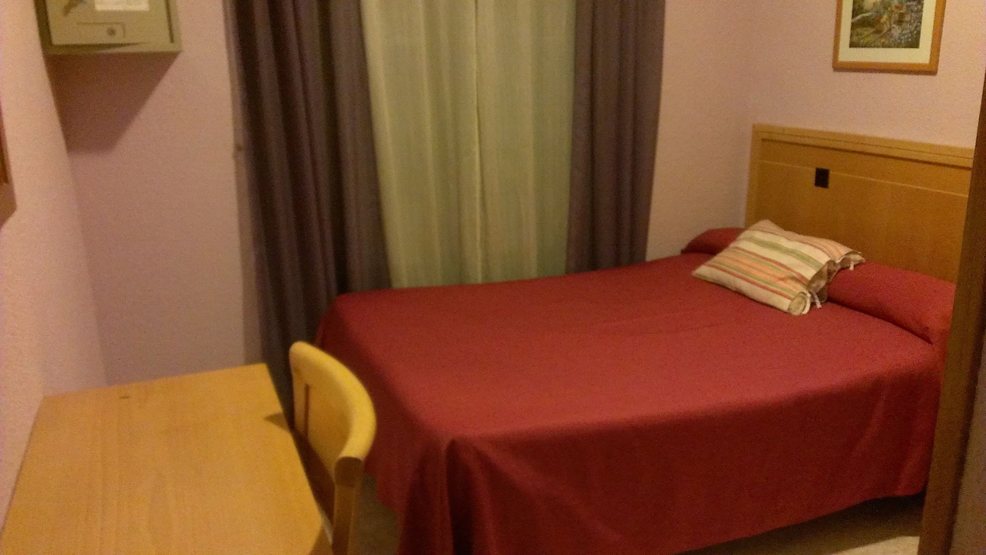 Une petite pièce avec un lit simple, une table en bois et une chaise.
