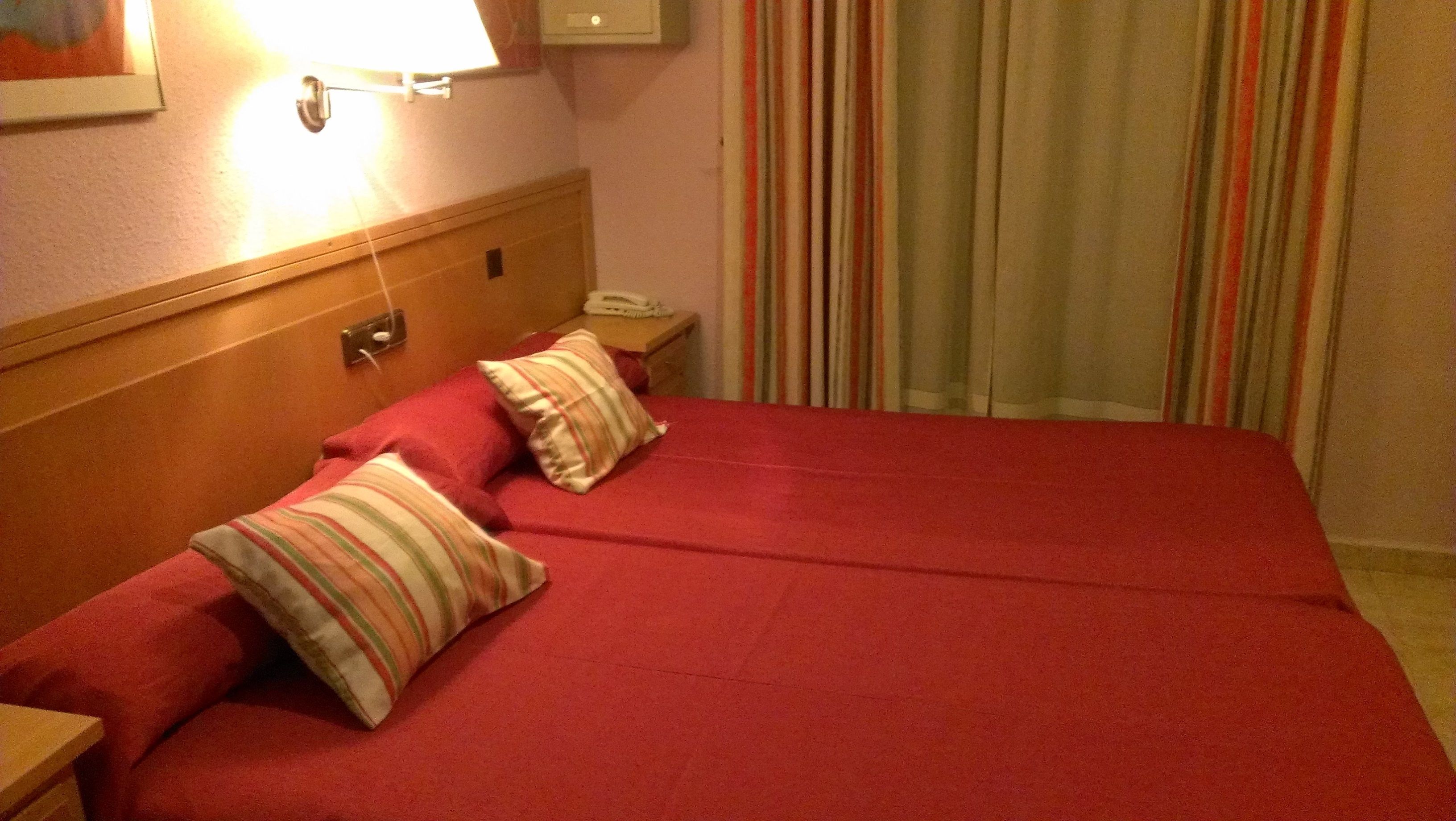 A hotel room with a bed, a nightstand, a lamp, and a telephone.