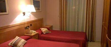 A hotel room with two beds, a bedside table with a lamp, a phone, and a picture on the wall.