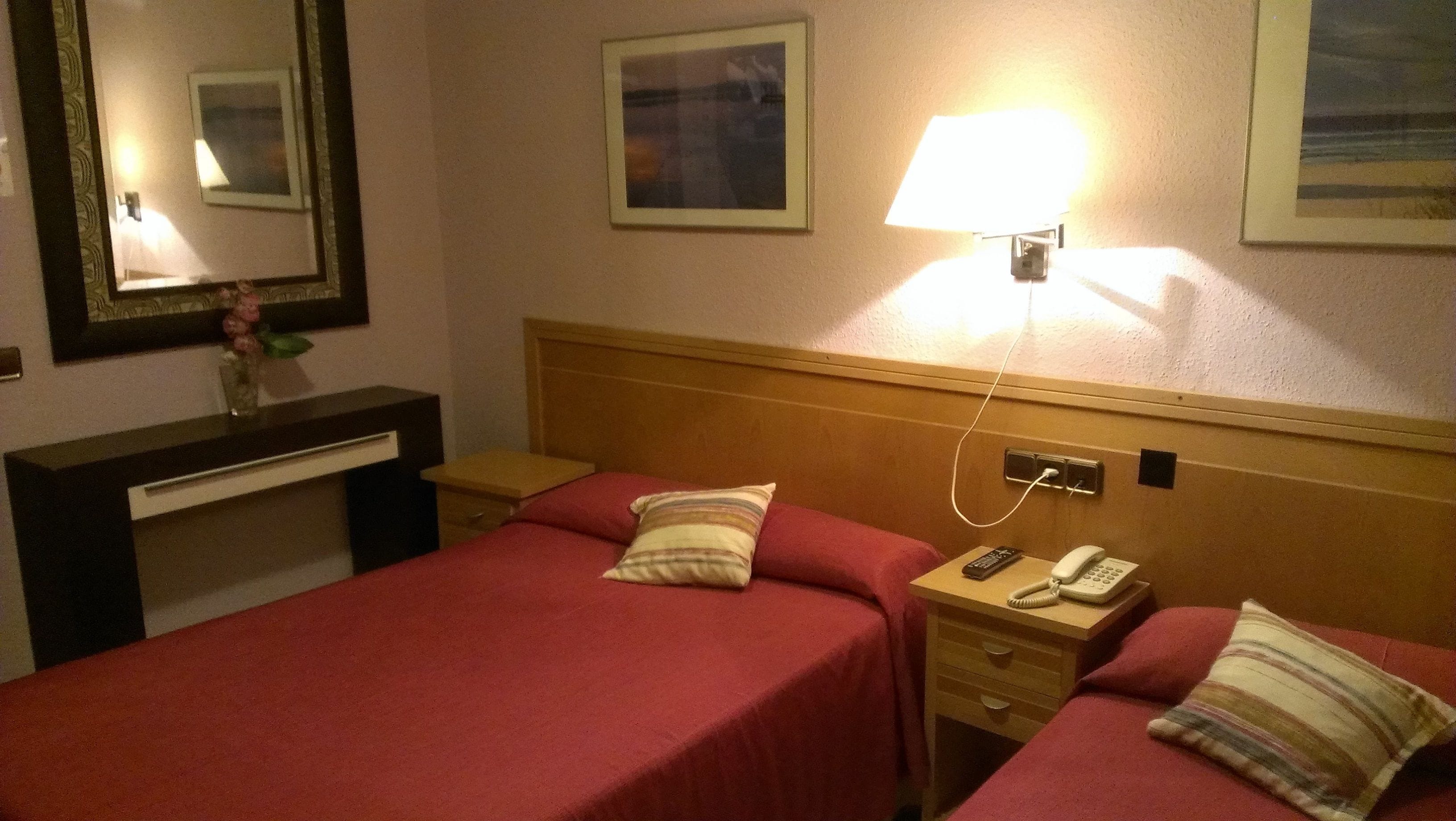 Habitación de hotel con dos camas, un escritorio, un espejo, una lámpara y un teléfono.