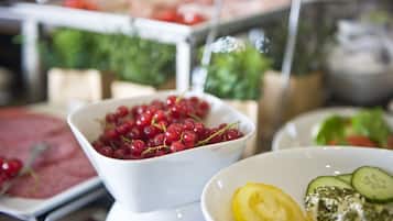 A buffet with various food items including a bowl of red berries, a dish with sliced cucumbers, and a creamy dessert.