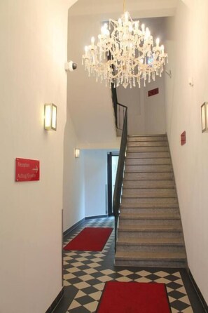 Vestíbulo de hotel con una escalera, una araña y un letrero de recepción.