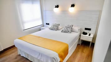 A hotel room with a bed, bedside tables, a nightstand, a window, and wall-mounted lights.