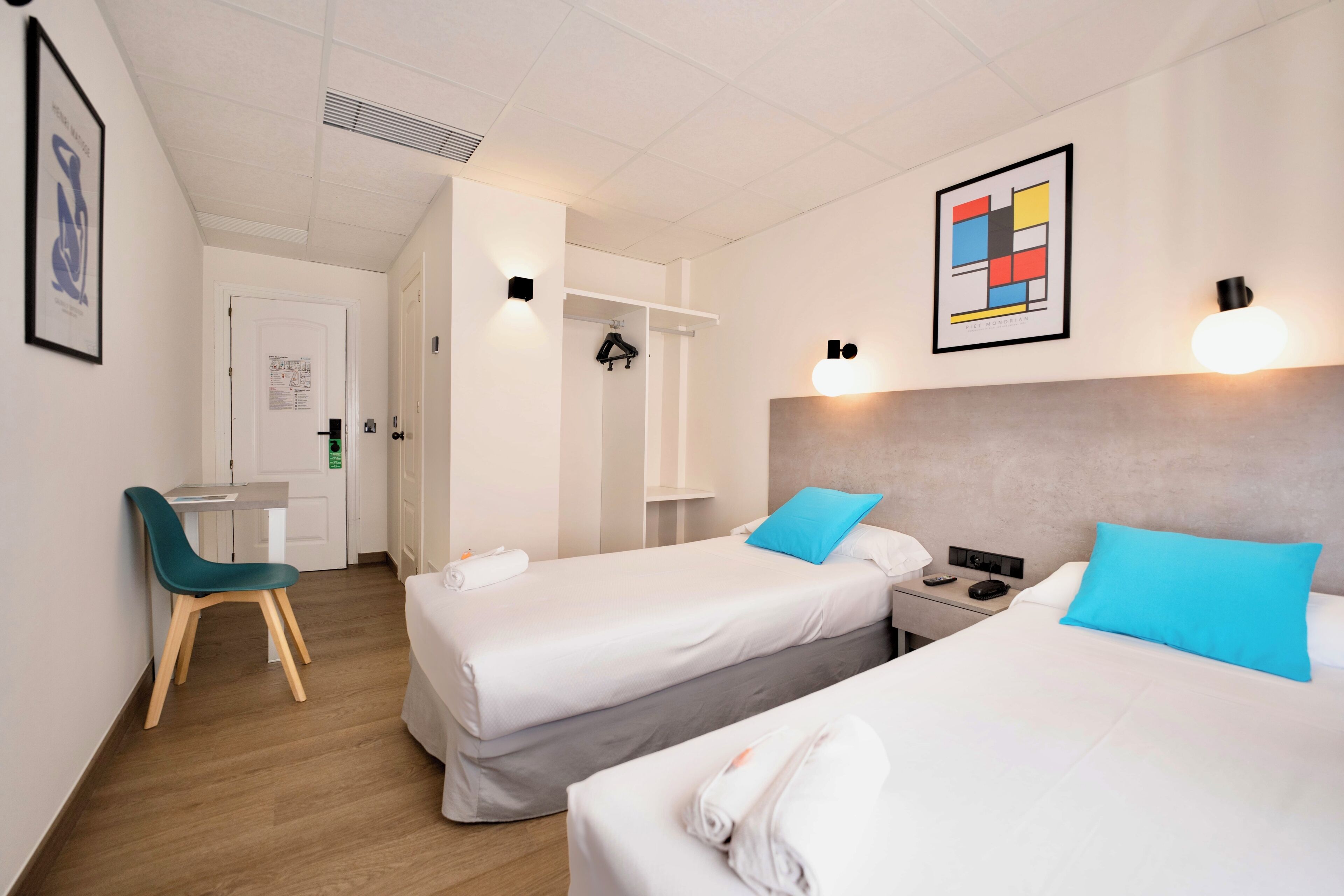 A hotel room with two beds, a desk, a chair, and a wardrobe.