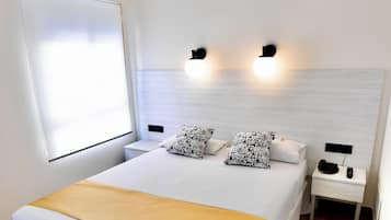 Una habitación de hotel con una cama grande, mesitas de noche, una ventana y lámparas fijadas a la pared.