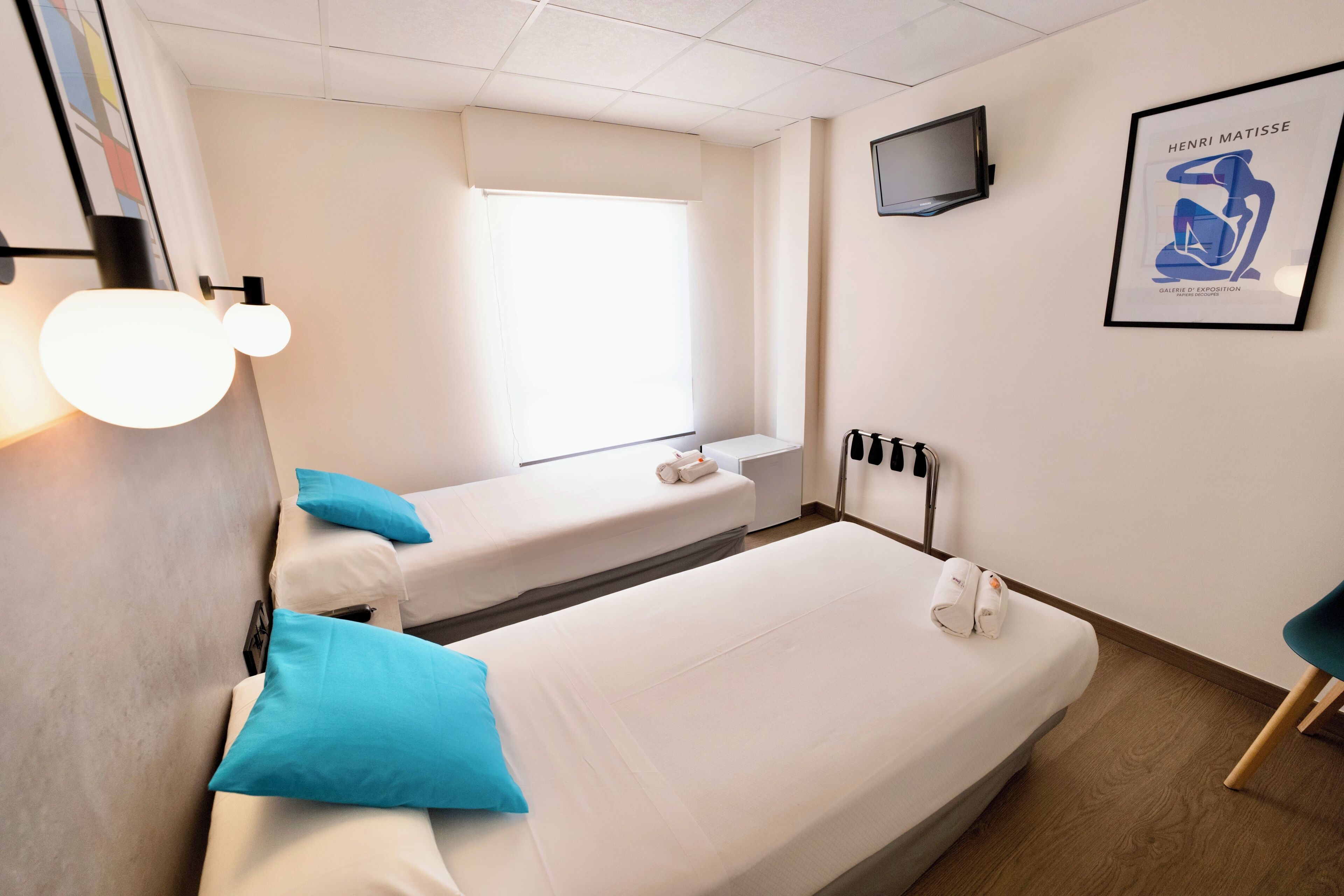 A hotel room with two beds, a television, and a framed artwork on the wall.
