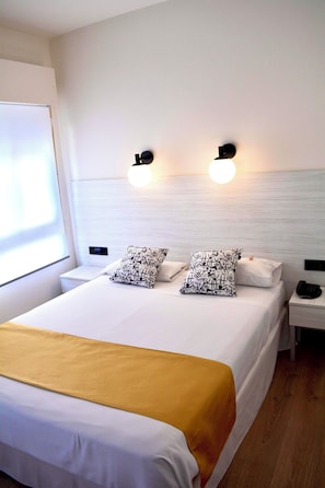 A hotel room with a bed, two bedside tables, a nightstand, and a wall-mounted light fixture. - Hotel Universal Murcia (Murcia)