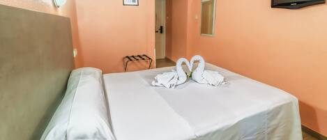 A hotel room with a bed, a television mounted on the wall, and a hallway leading to another room.