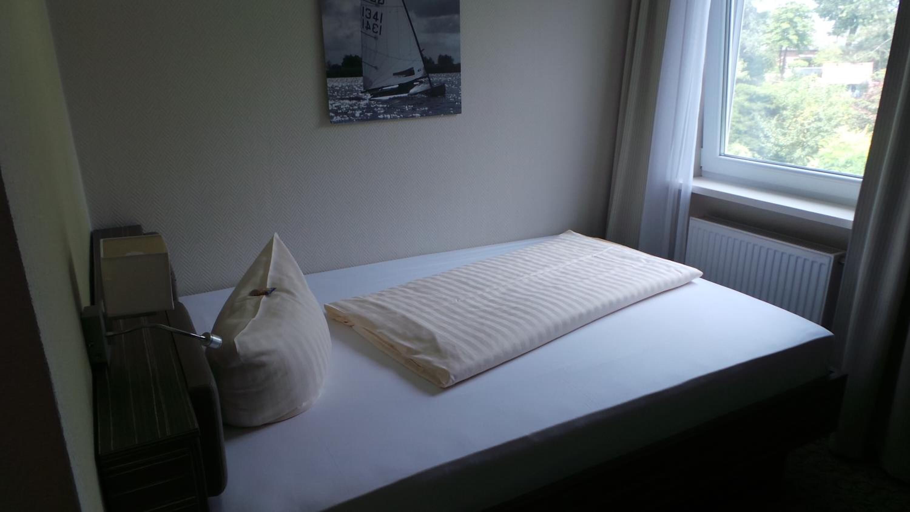 A small, single-bed room with a window, a radiator, and a wall-mounted poster.