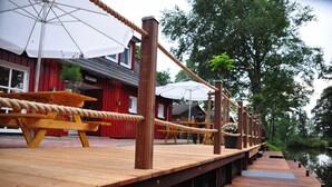 Una terraza de madera con barreras de cuerda, mesas de picnic y sombrillas.