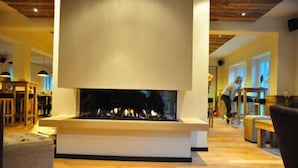 Una sala de estar moderna con chimenea, piso de madera y una persona al fondo.
