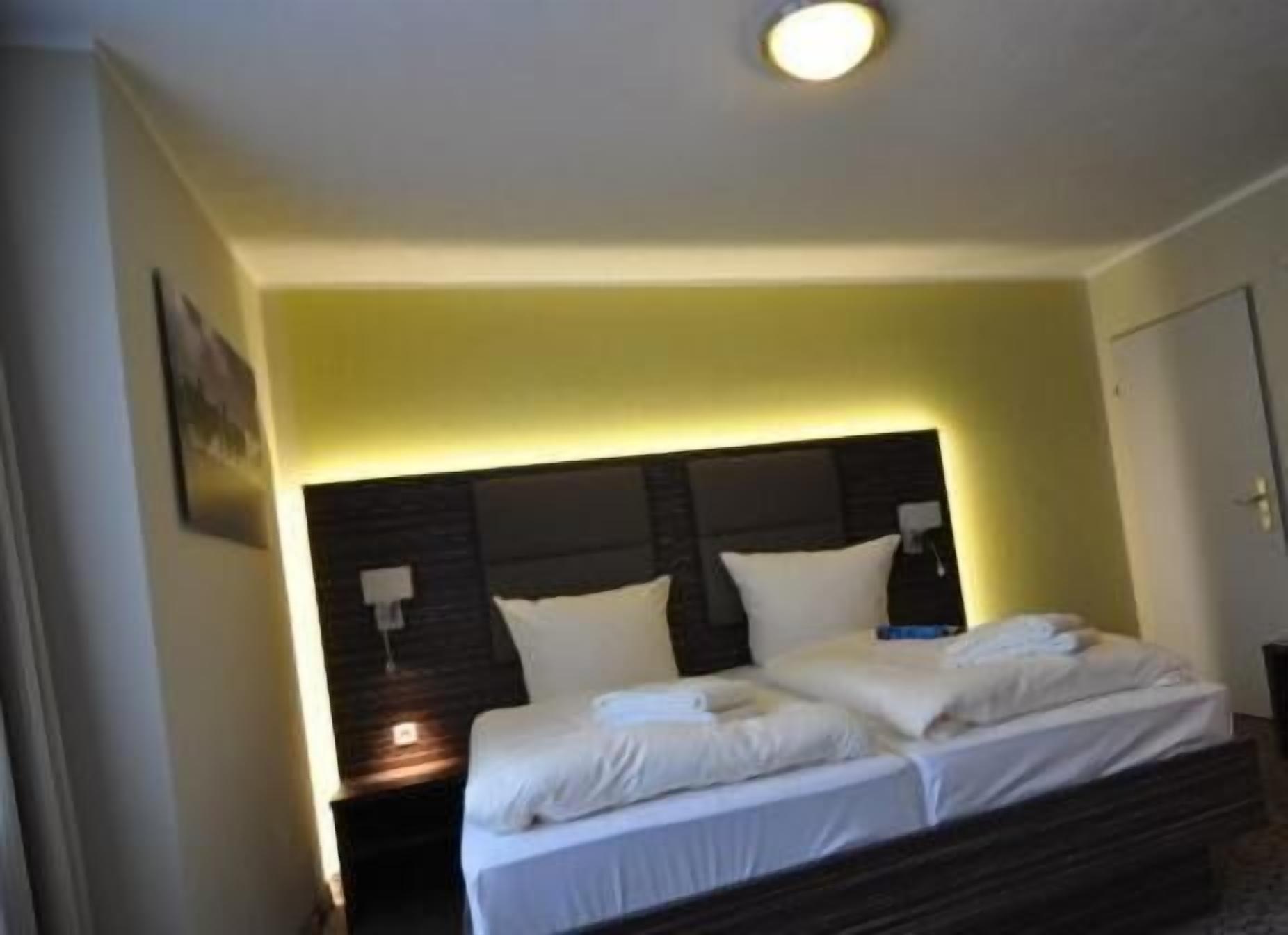 Un lit double avec du linge de lit blanc, une tête de lit sombre et une table de chevet avec une lampe.