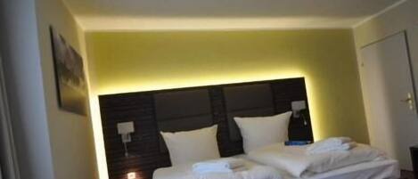 Un lit double avec du linge de lit blanc, une tête de lit sombre et une table de chevet avec une lampe.