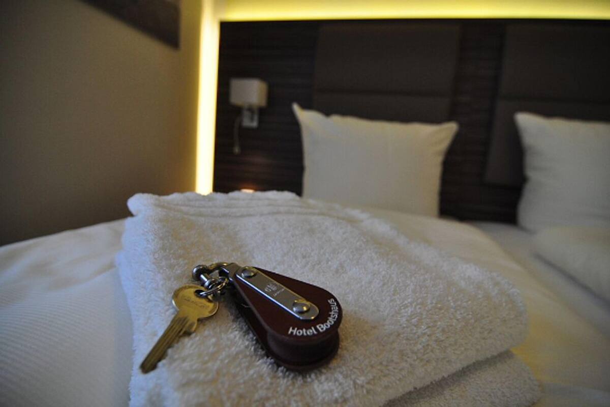 A neatly made bed with a white towel and a keychain labeled "Hotel Bookmarks" on it.