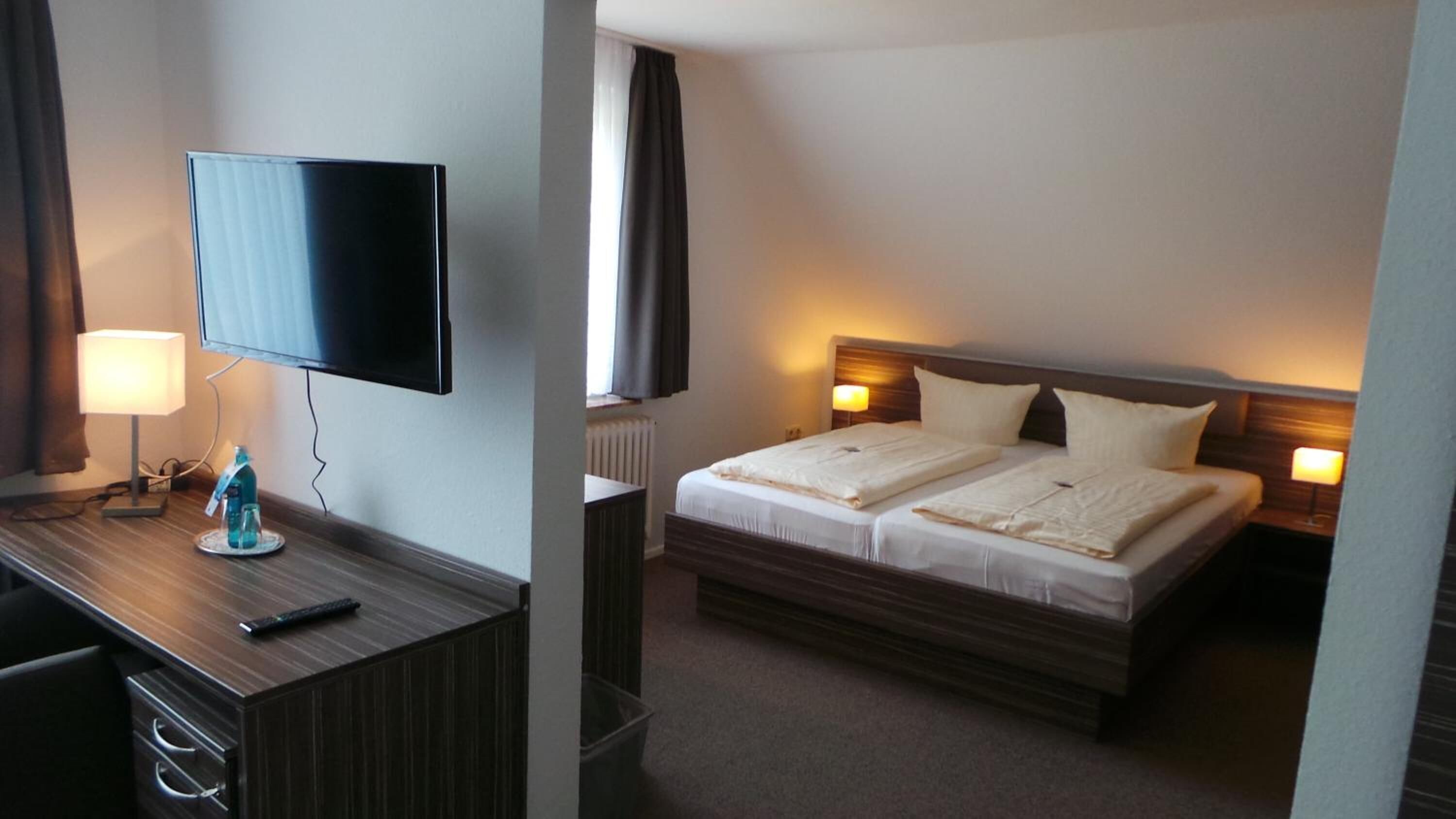Una habitación de hotel con televisión en un escritorio, una cama con dos almohadas y lámparas de noche.