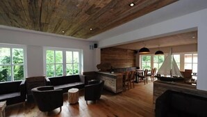 Amplia sala de estar con techo de madera, ventanas grandes, zona de cocina y una maqueta de un velero.