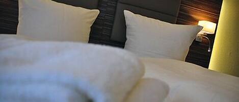 A hotel room with a neatly made bed, a headboard with a light fixture, and a nightstand with a lamp.