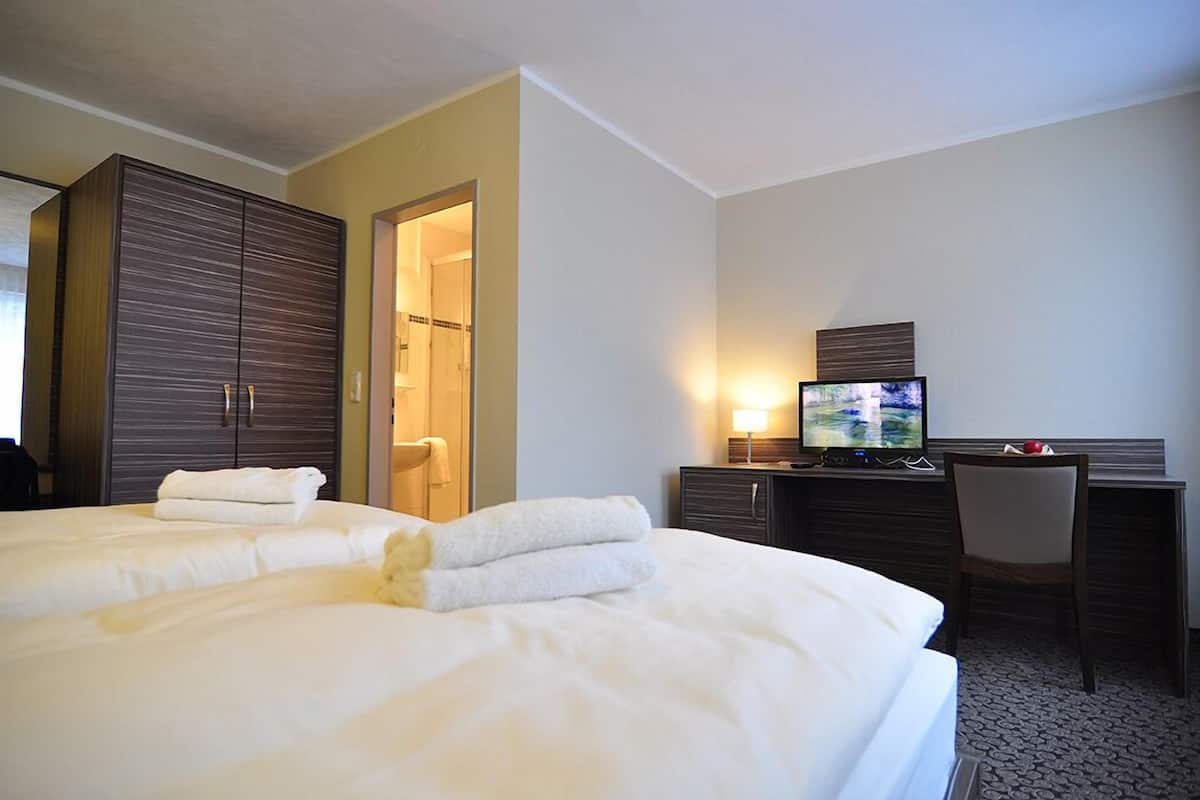 A hotel room with a large bed, a desk with a computer, a TV, and a wardrobe.