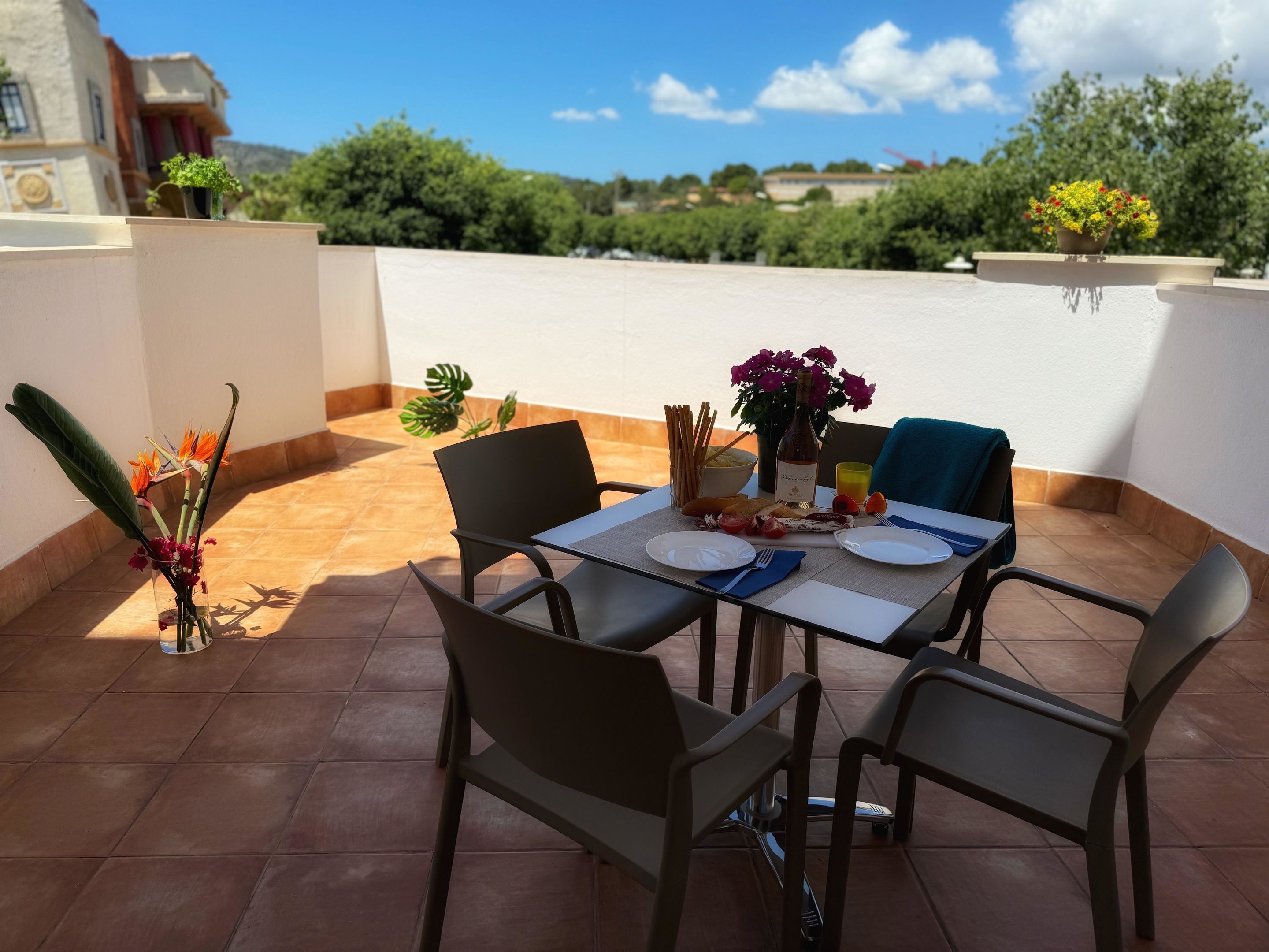 Una terraza con una mesa dispuesta para dos personas, con una botella de vino, pan y un frutero.