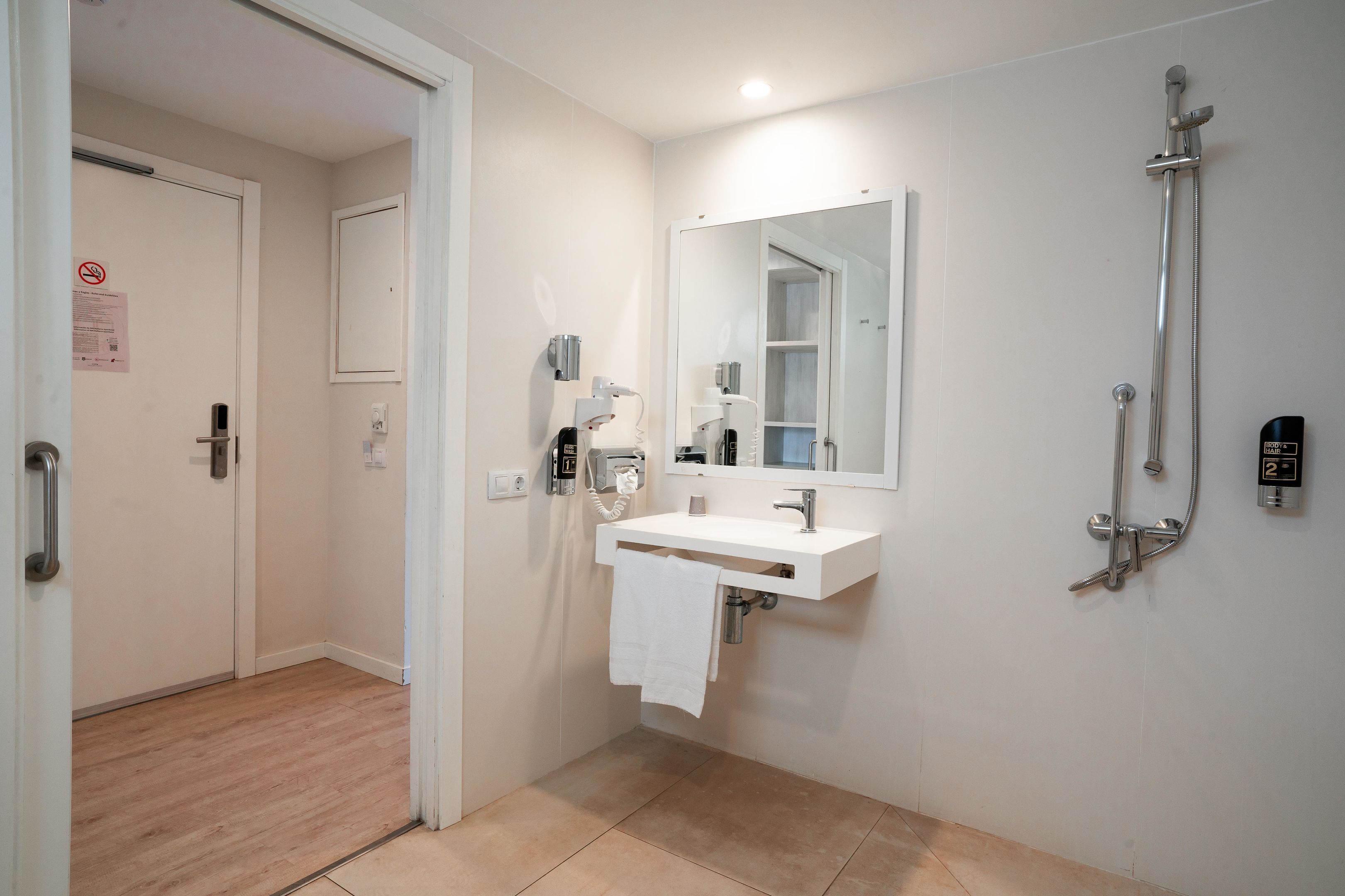 Een moderne badkamer met een witte wastafel, een spiegel, een handdouche en een handdoek aan de muur.