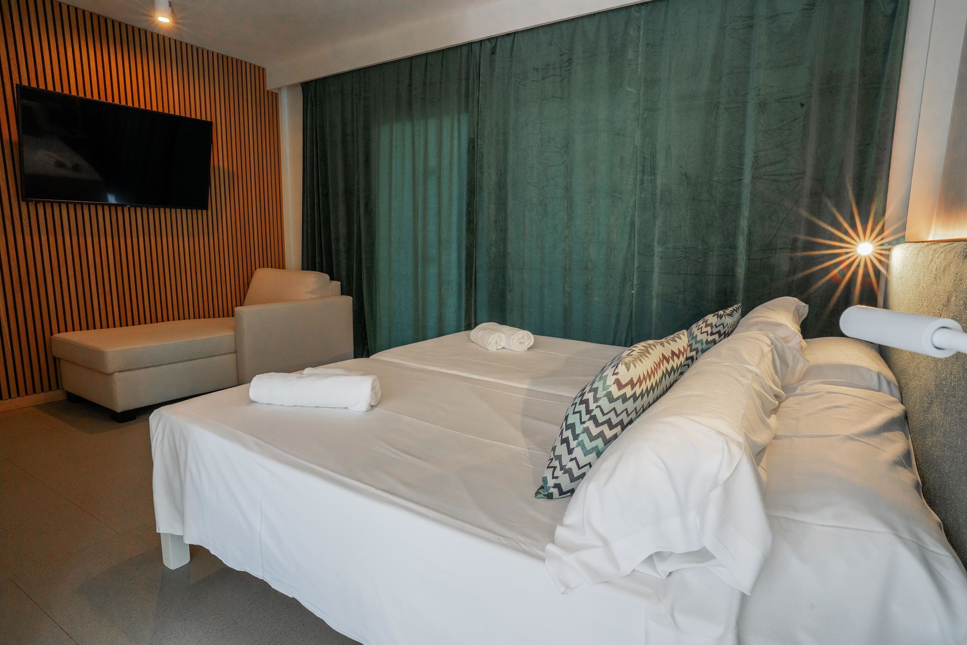 A hotel room with a bed, a sofa, a TV mounted on the wall, and a curtain.
