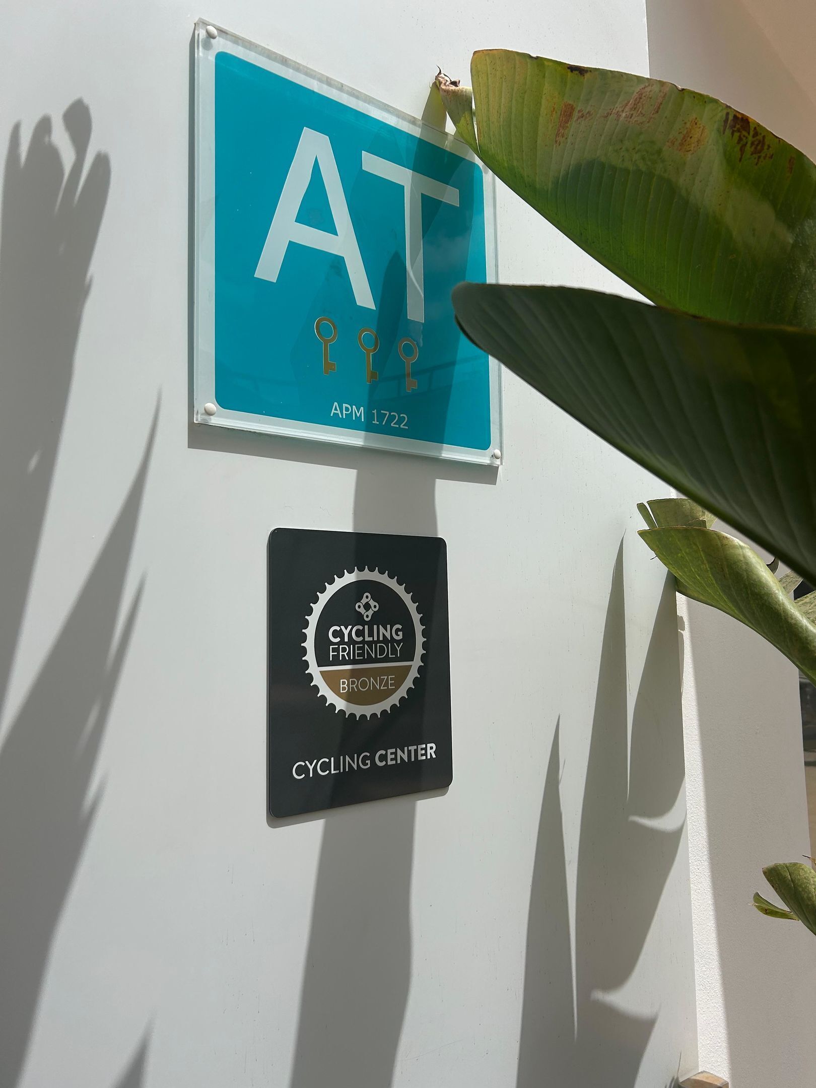 A blue sign with 'AT' and 'APM 1722' on a white wall, and a 'Cycling Friendly Bronze' sign below it.