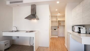 A modern kitchen with a built-in stove, sink, and microwave. There is a small refrigerator and a dish drying rack. The kitchen has wooden flooring and white cabinetry.