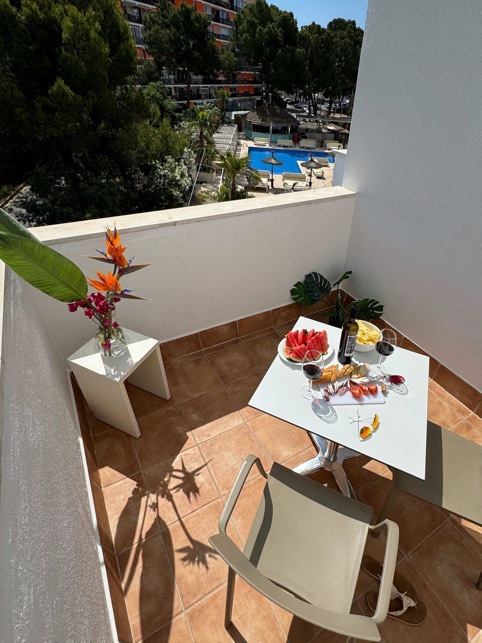 Un balcón con una mesa dispuesta para una comida, una silla y una planta en maceta.