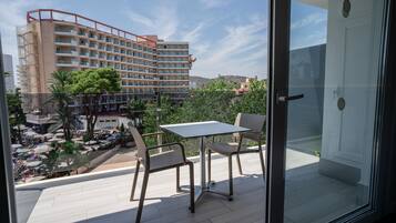 A balcony with a table and chairs, overlooking a pool area and a hotel building.
