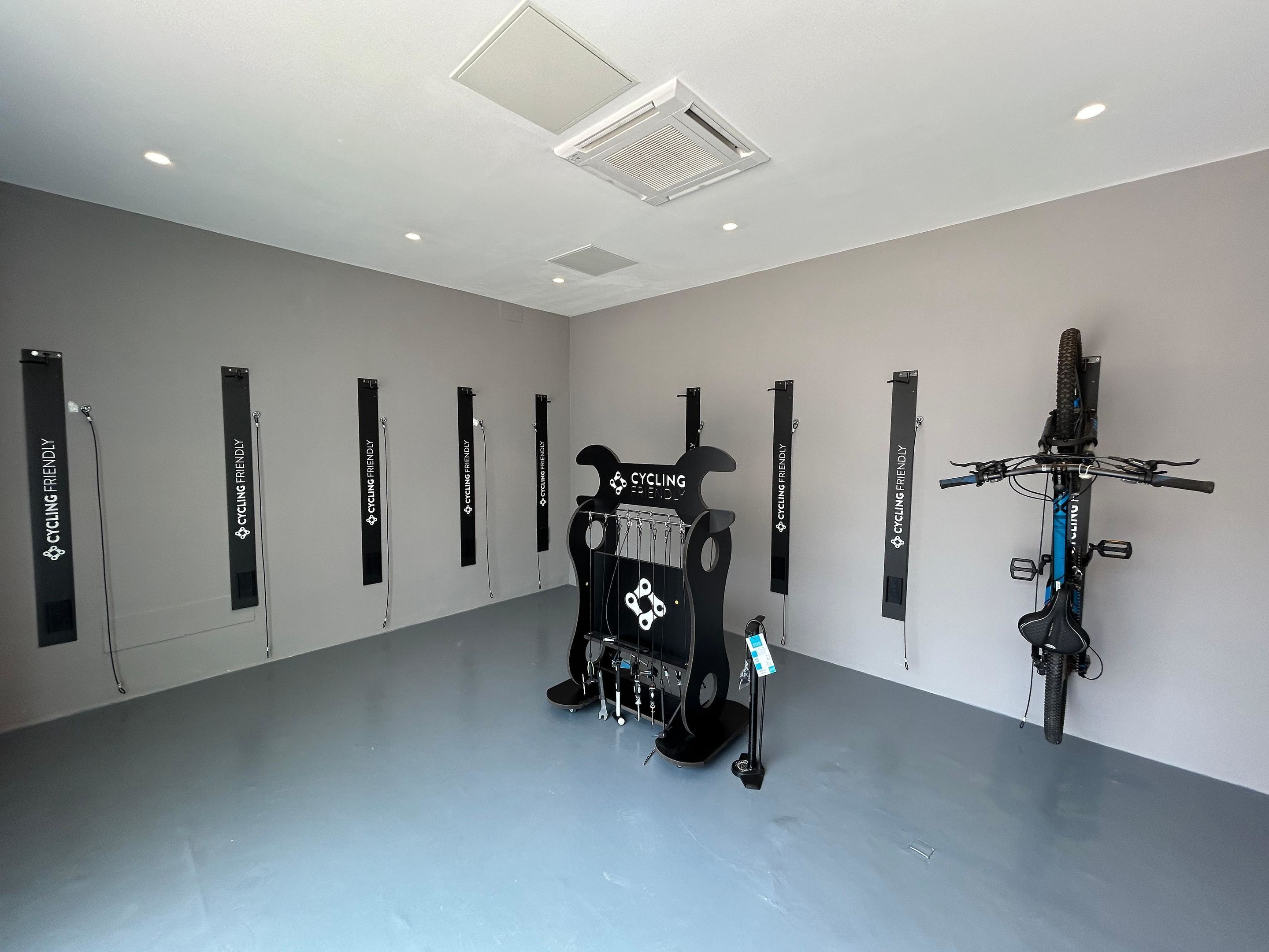 A spacious room with a grey floor and white walls, featuring a black bicycle and a bike rack with multiple bikes.